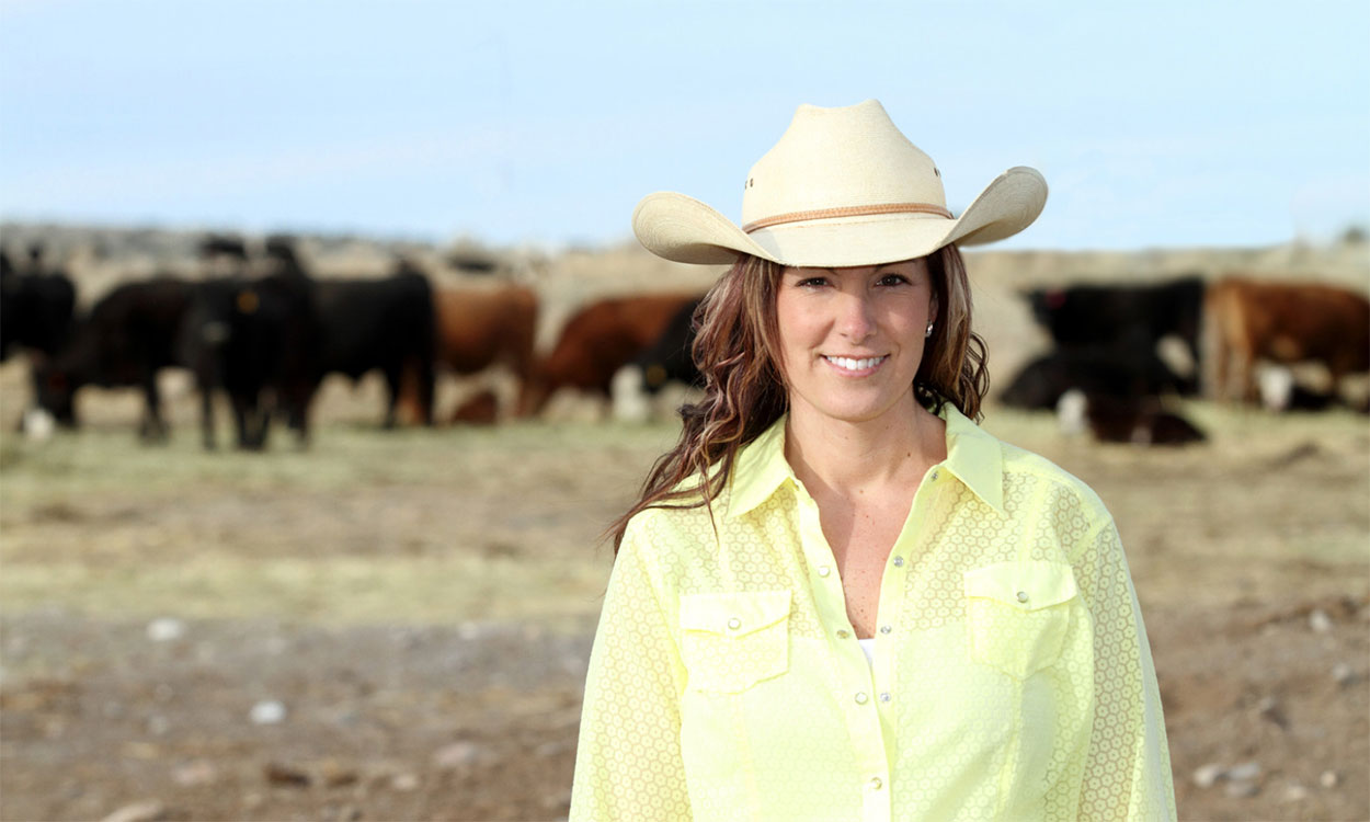 Female rancher standing in front of a cowherd.