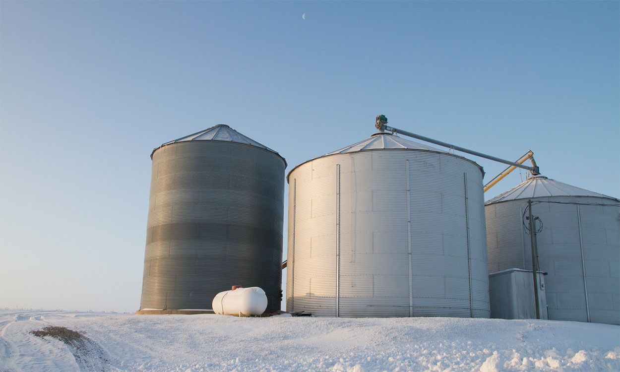 Three grain bins on the edge of a snow-covered field.