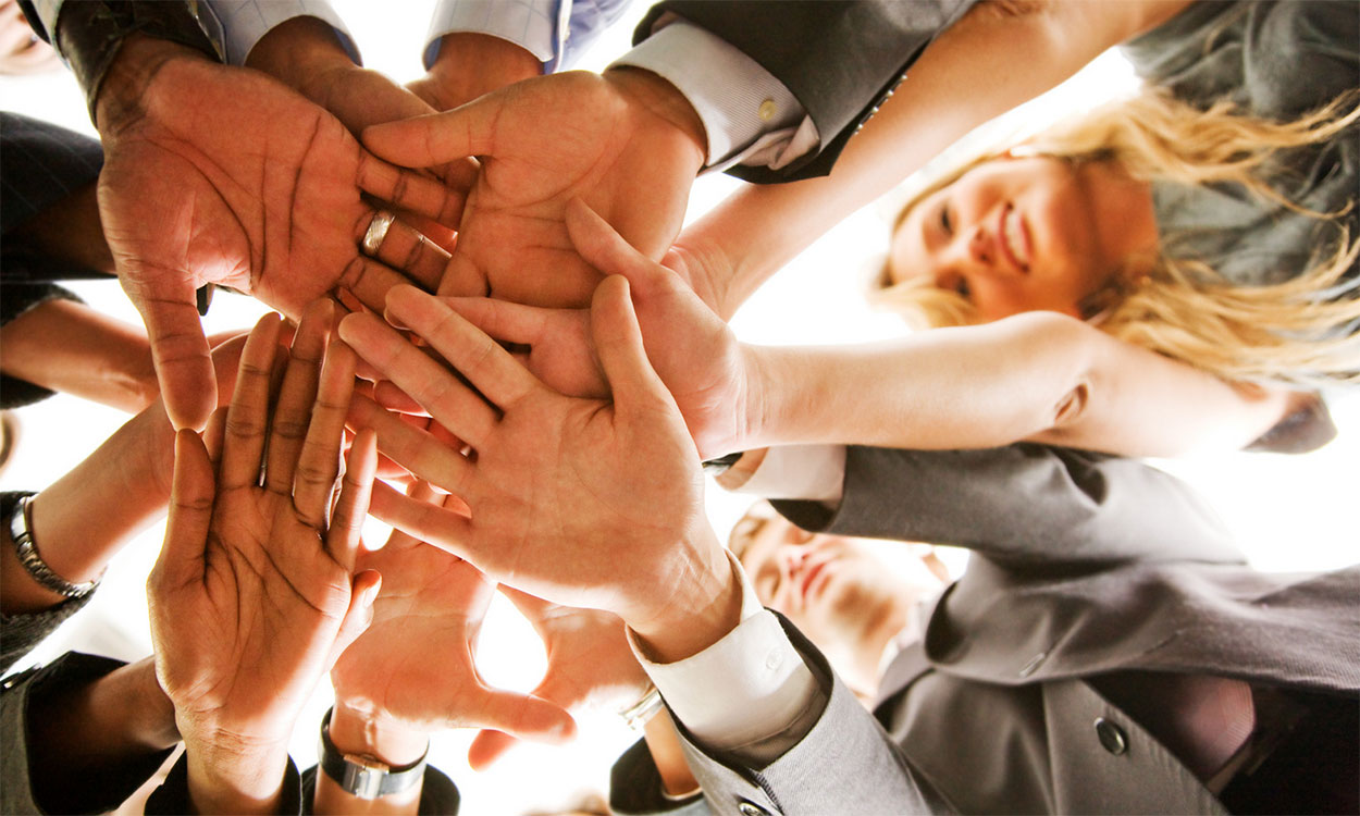 Diverse group of young professionals putting their hands together in a huddle.