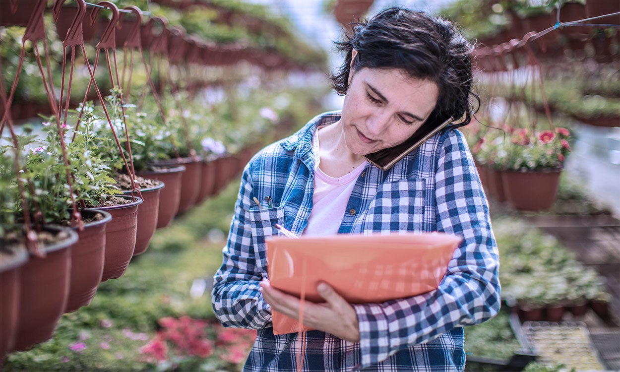 Female gardener with clipboard and phone in a greenhouse.