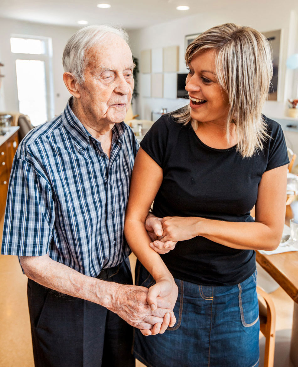 Older adult man getting assistance from a young, female caregiver.