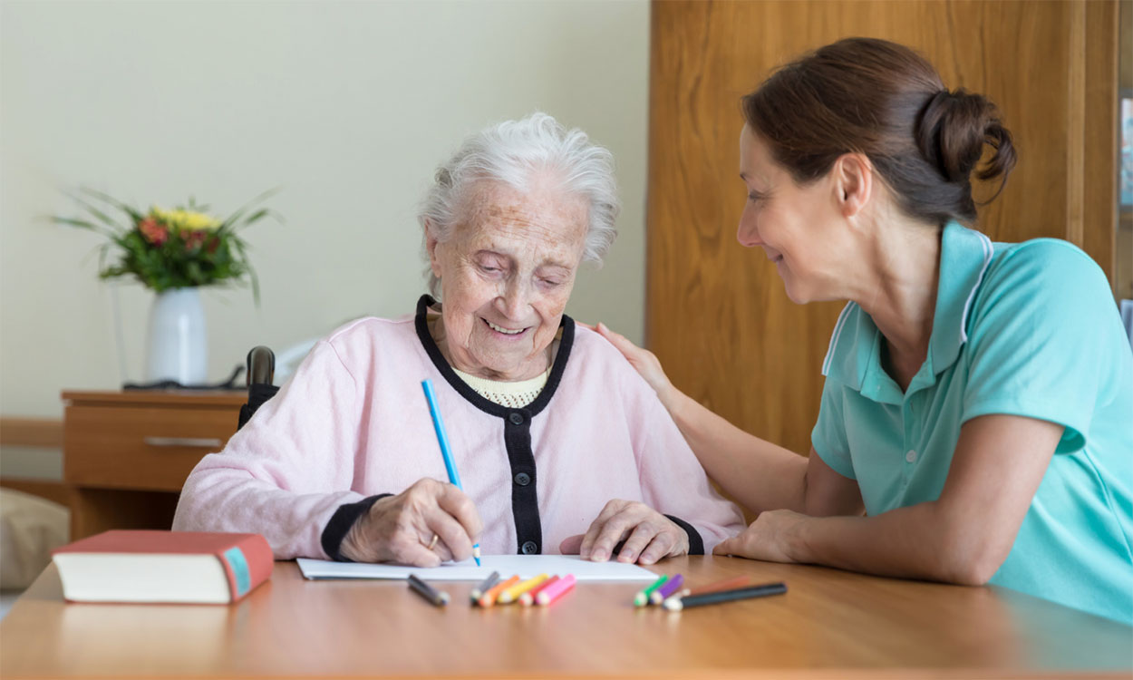 Caregiver assisting an older adult woman through a memory exercise.