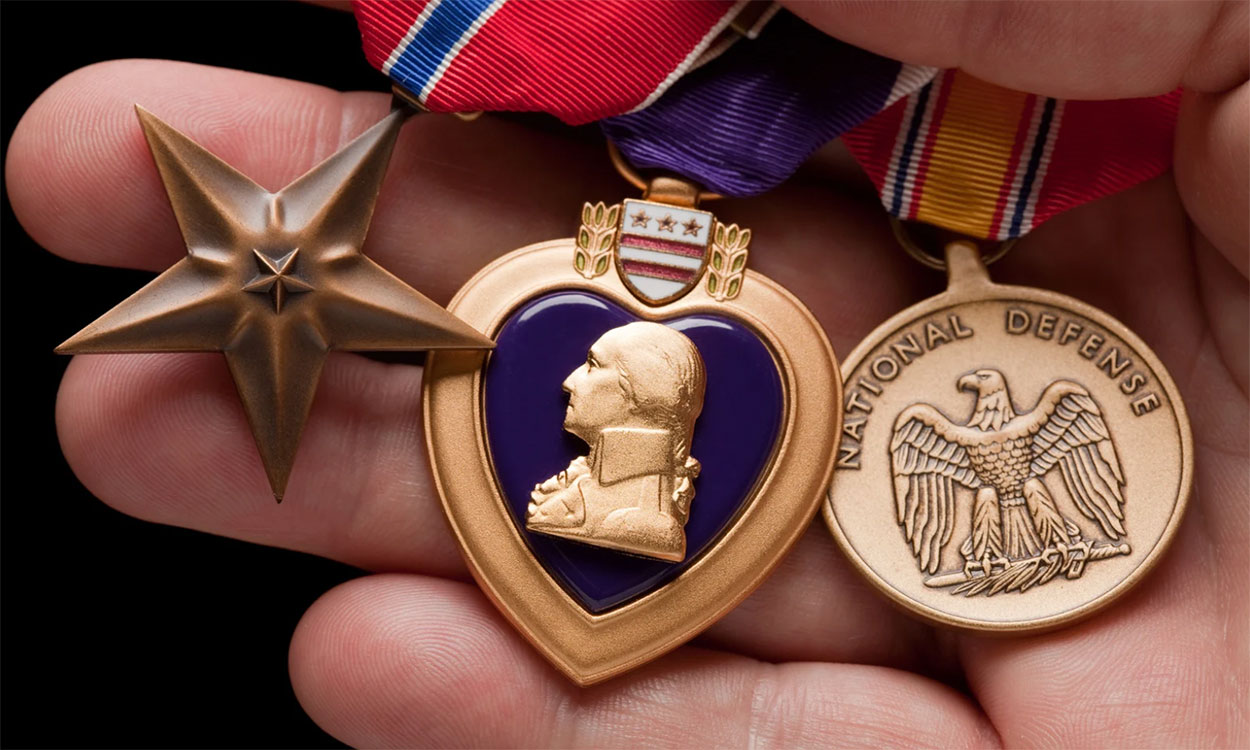 Hand holding Purple Heart, Bronze and National Defense War Medals.