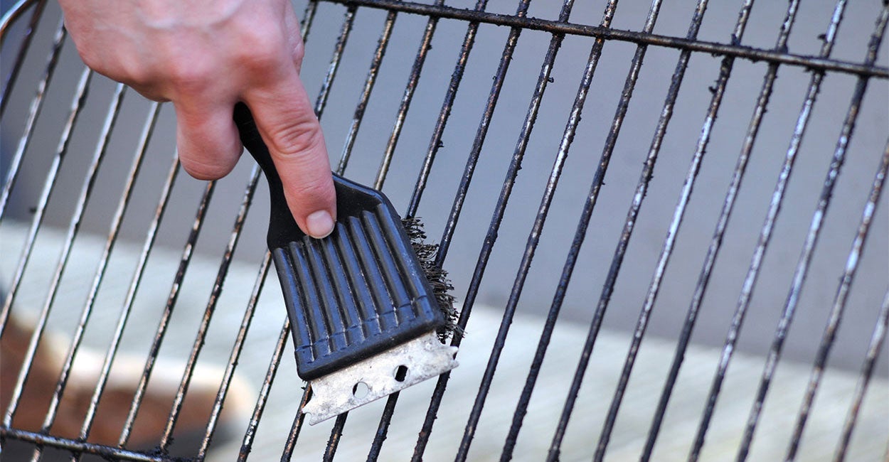 Hand cleaning a removed grill grate with a wire brush.