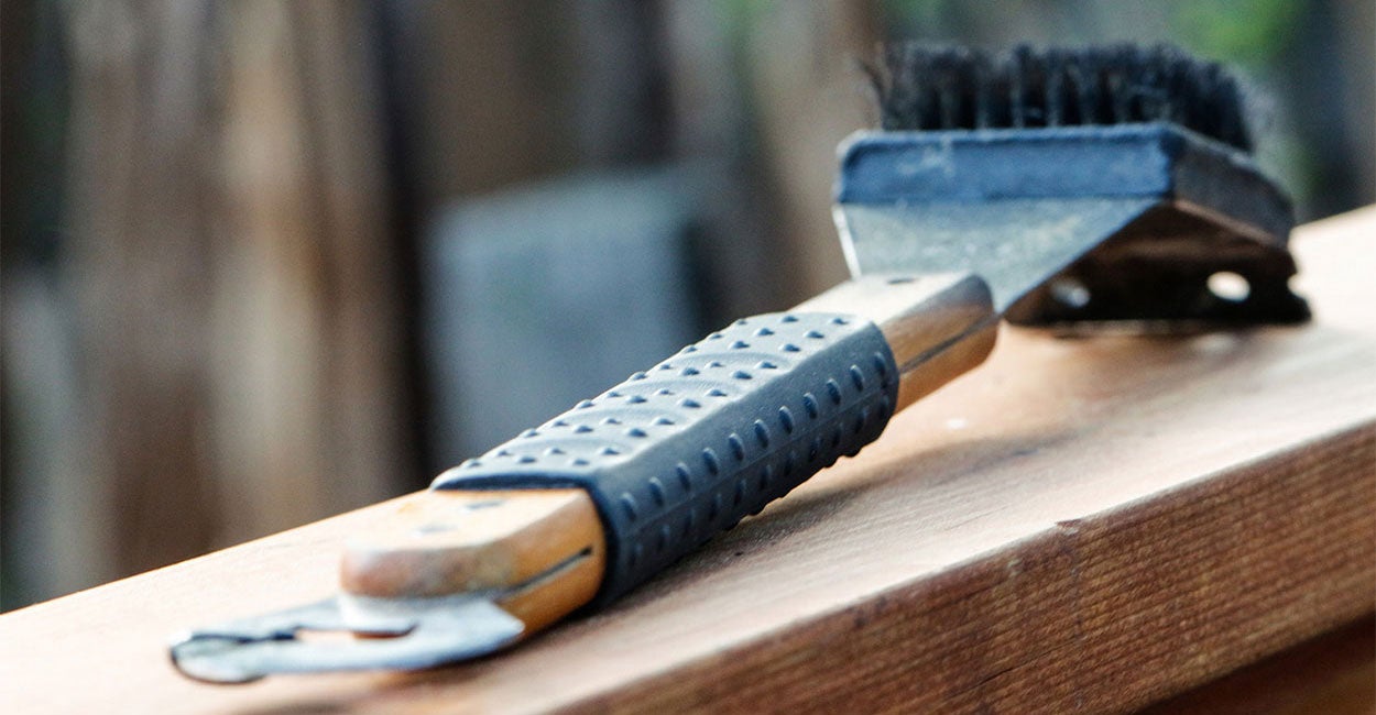 Grill brush sitting on wood deck railing.