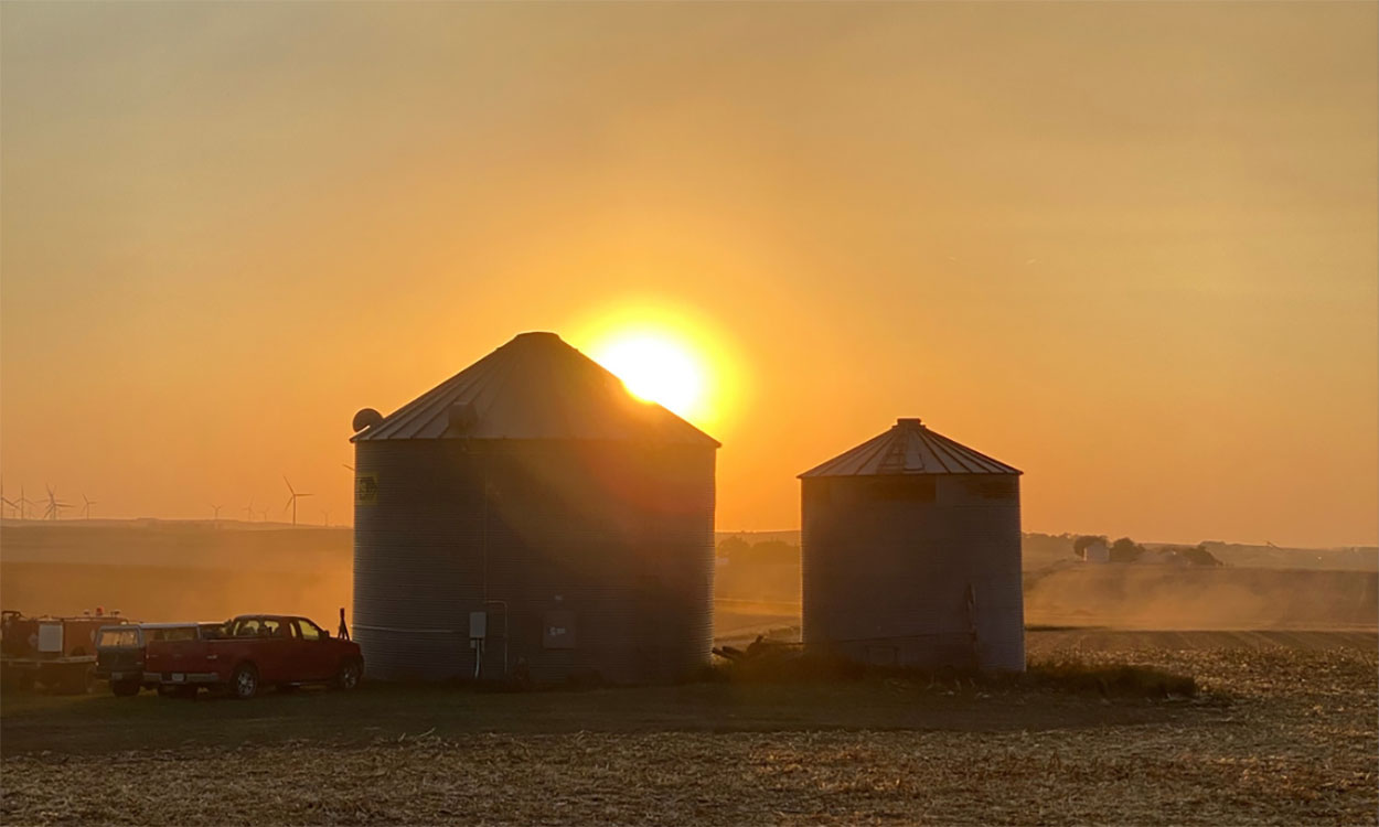 Sunset over two grain bins in a field.