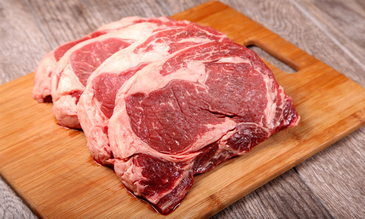 Three ribeye steaks on a cutting board.