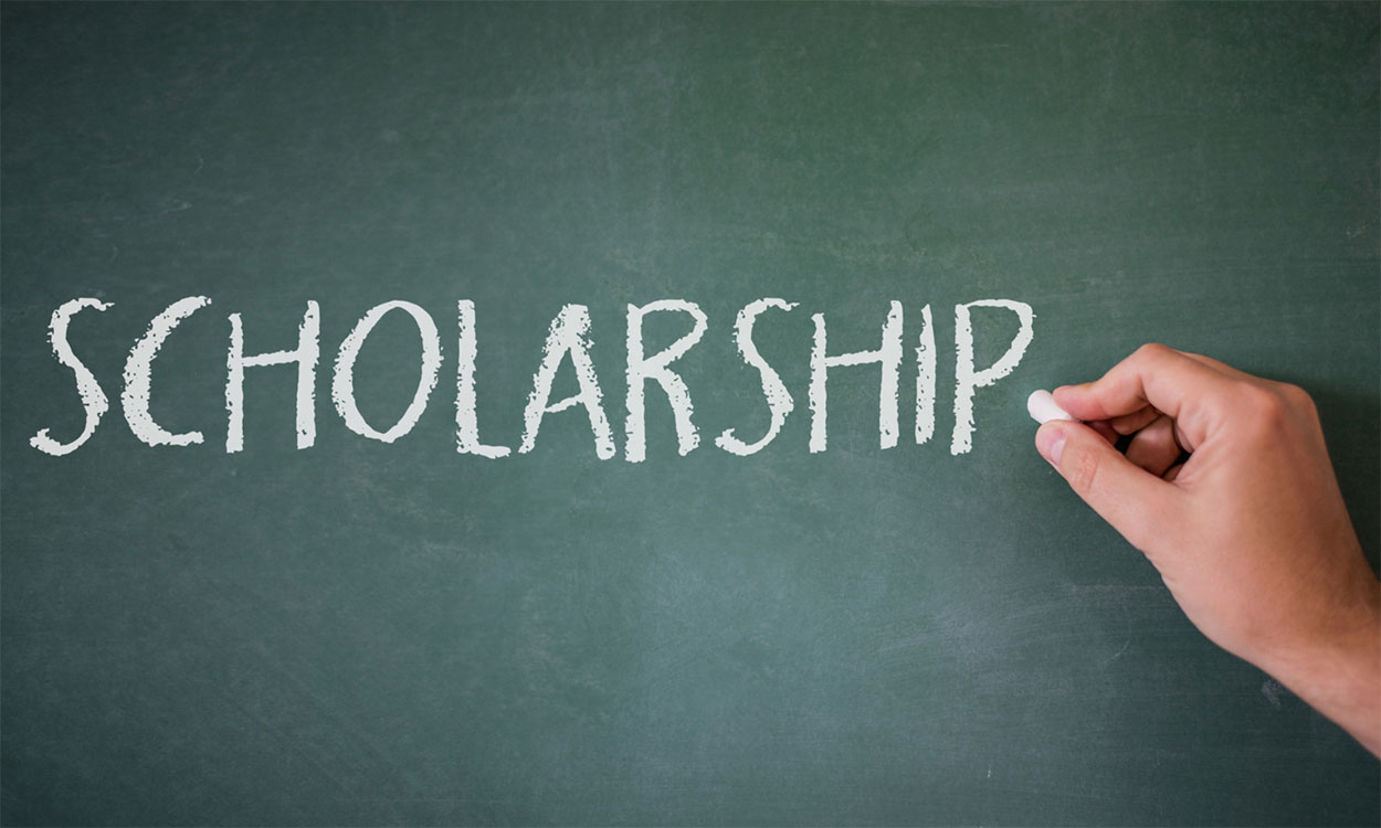 Hand writing the word “scholarship” on a chalk board.