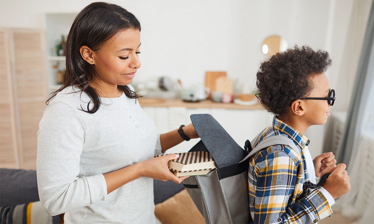 Mother helping her son prepare his school backpack.