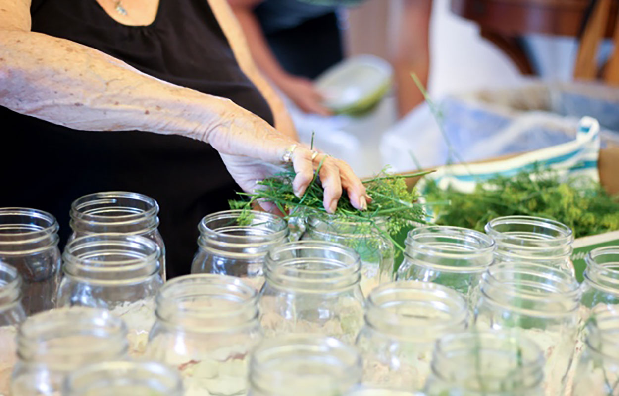 Woman preparing fresh herbs for canning in glass jars.