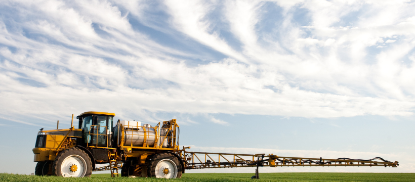 Sprayer in a field with a blue sky and wispy clouds on the horizon