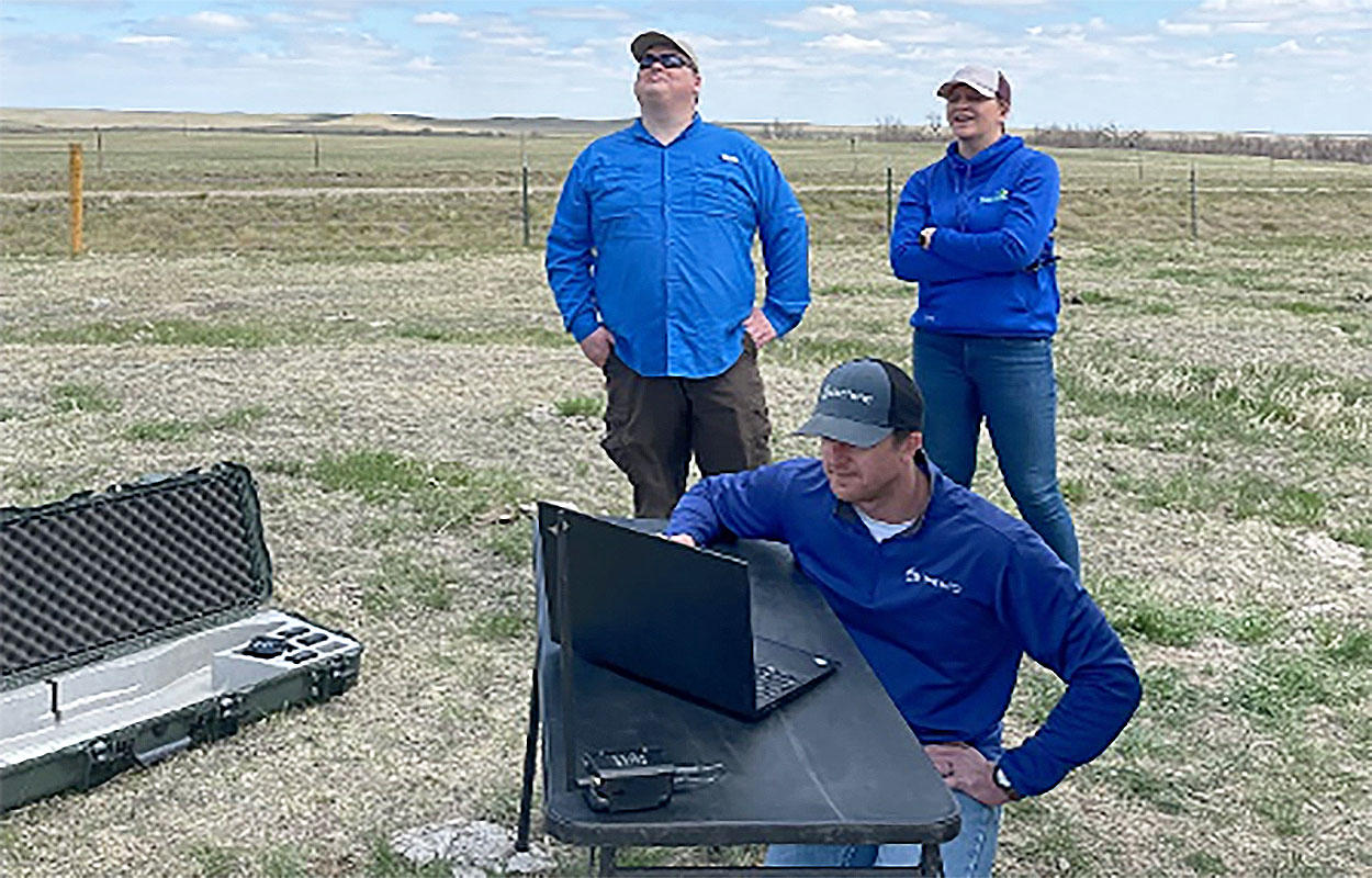 People standing in field observing a drone flight.