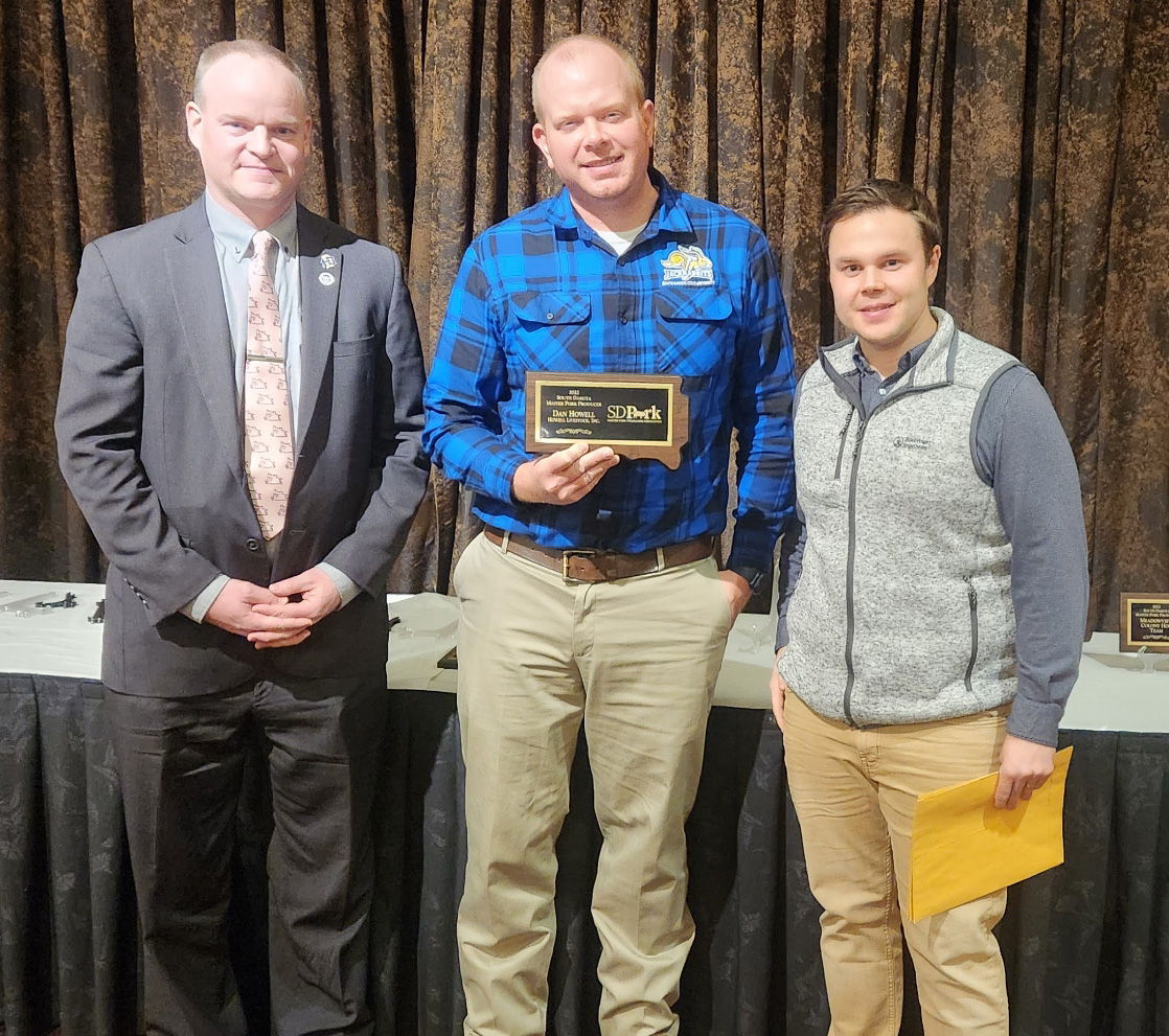 Three men stand in a row, and the man in the middle, Dan Howell, displays a plaque he won from South Dakota Master Pork Producers