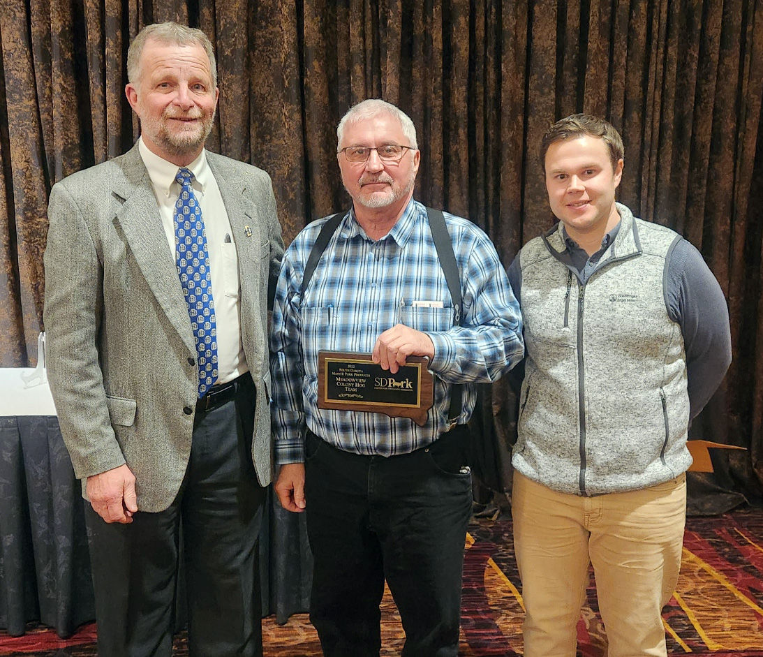 Three men stand in a row, and Steve Waldner stands in the center displaying the plaque he won from South Dakota Master Pork Producers