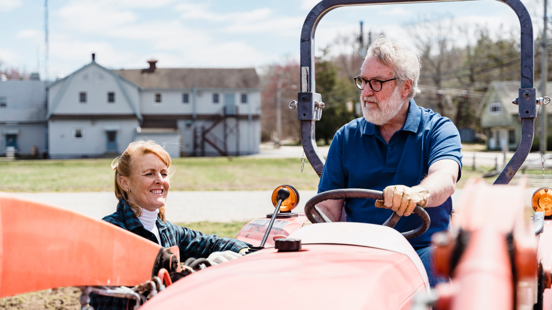 An older man sitting on a tractor with his wife standing on the ground talking to him