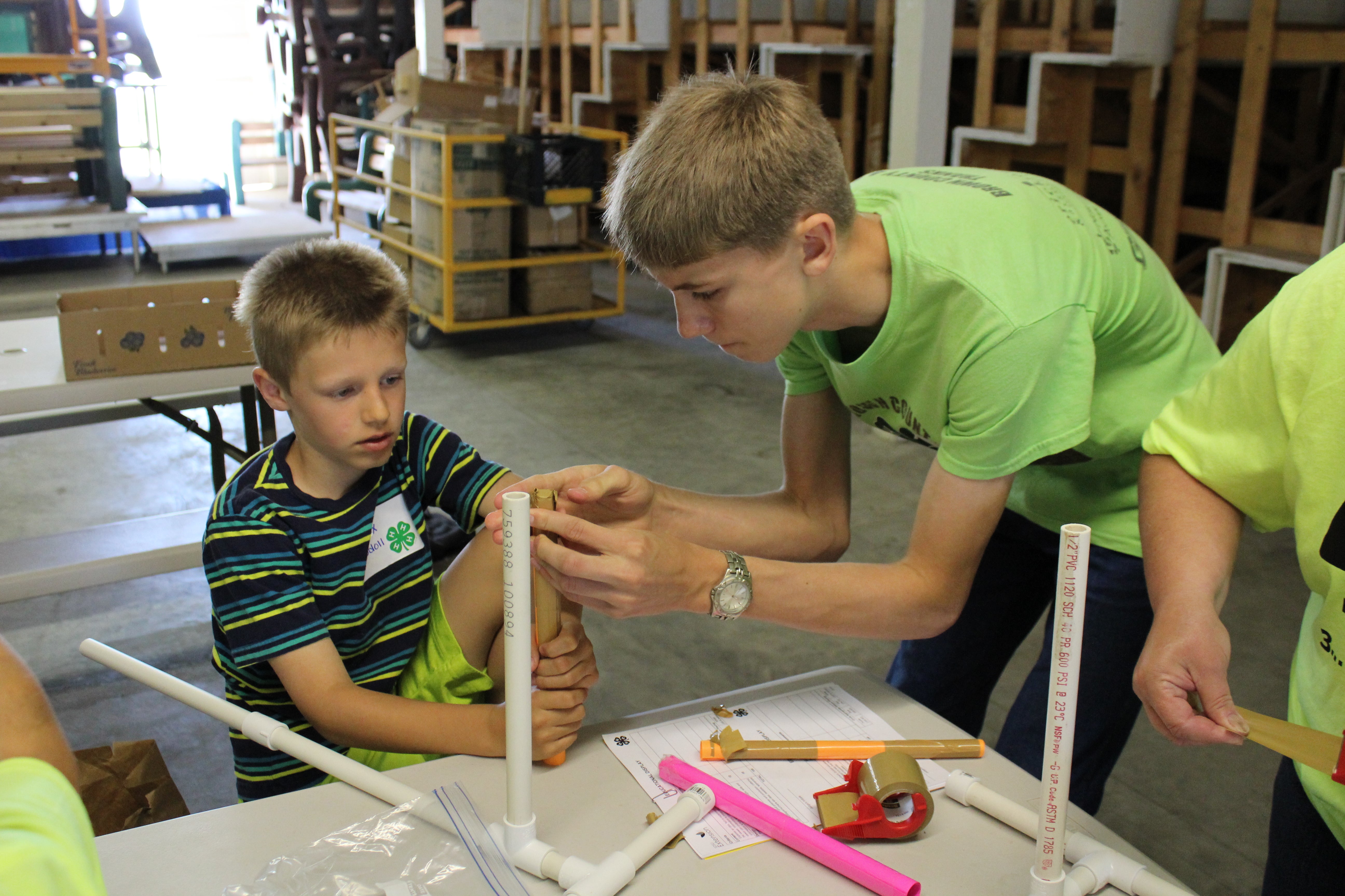 Male 4-H member helping a younger male put tape on a PVC pipe for a project