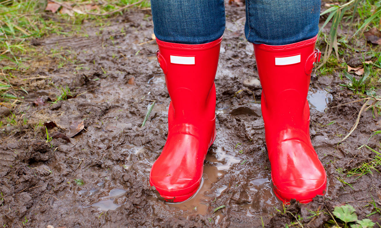 Gardener in red rain boots standing in a wet yard.