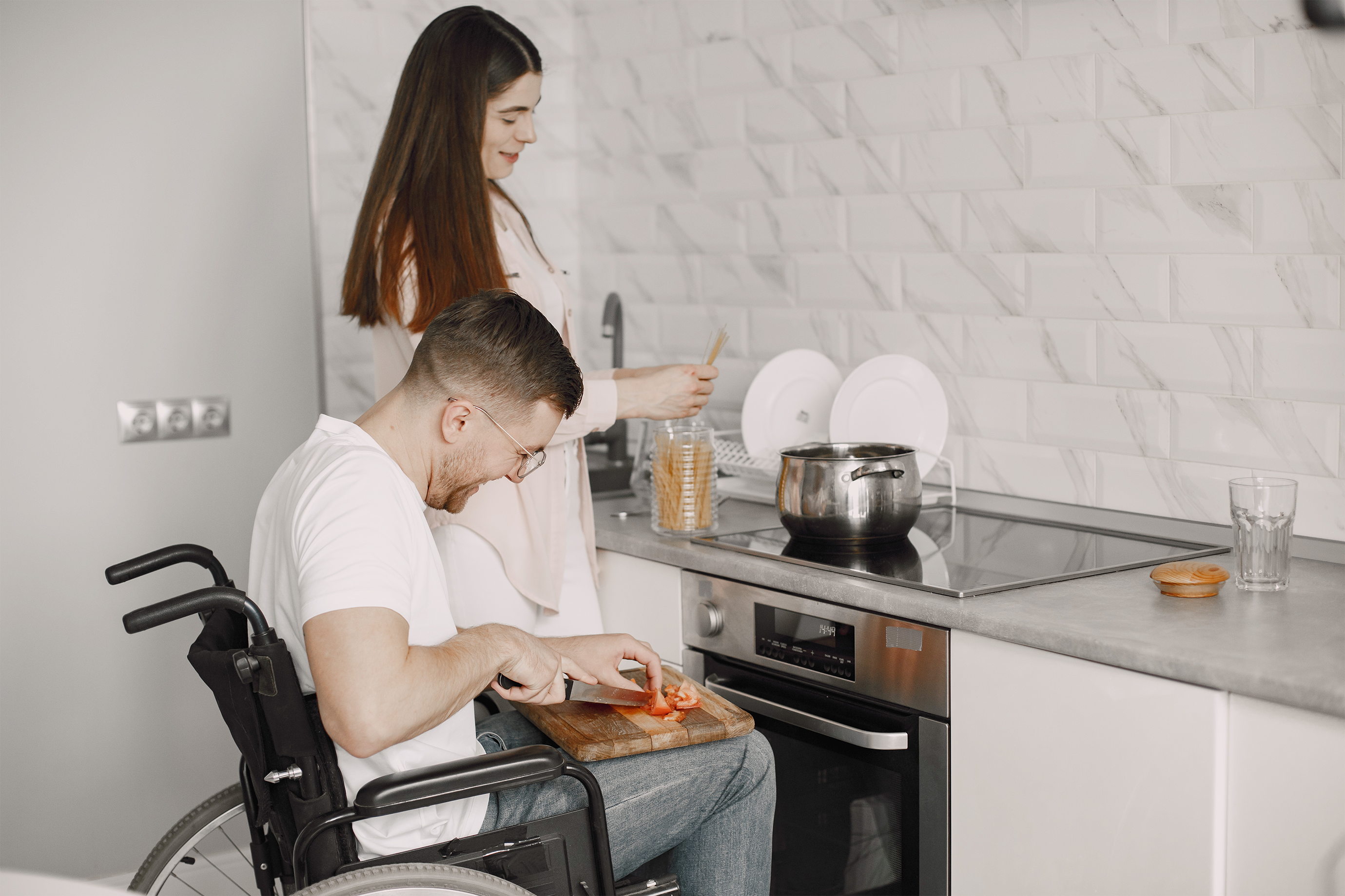 Man in a wheelchair cooking in an accessible kitchen with a woman.