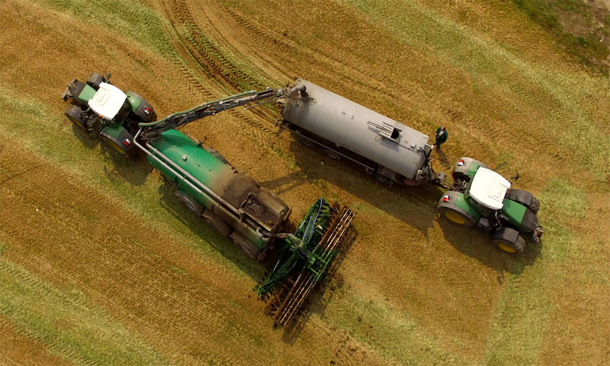 Tractor loading a liquid manure applicator in a bare field.