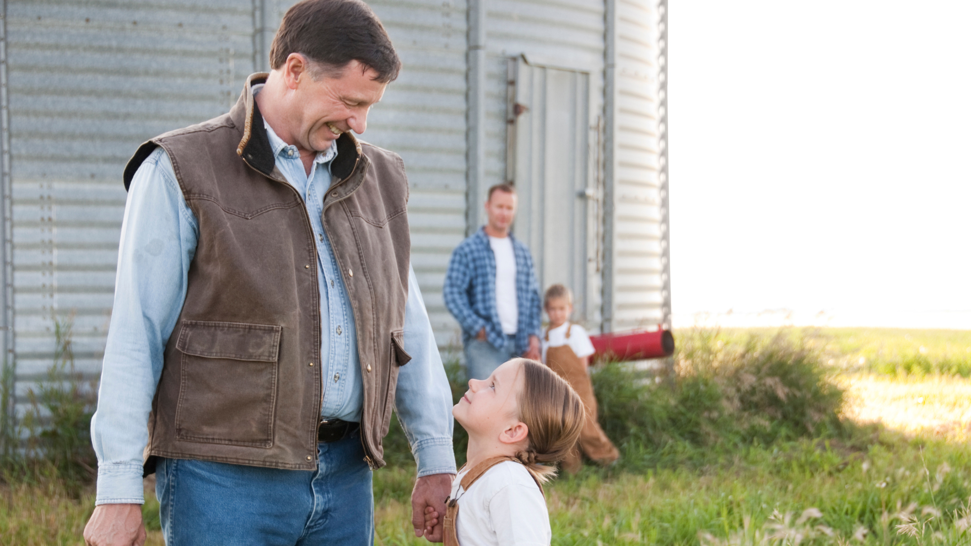 Older adult looking holding hands with young girl, while a father and son look on from a distance