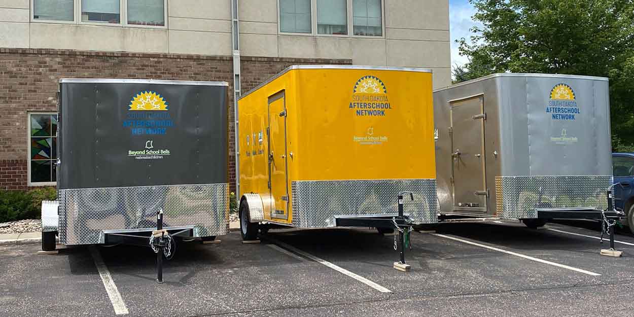 Three Think, Make, Create mobile lab trailers are parked in a lot with a building behind them.