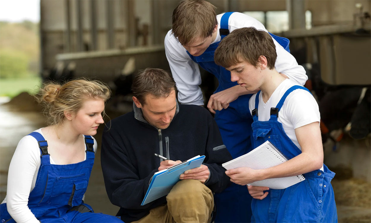 Group of farm trainees gathered around a veterinarian.