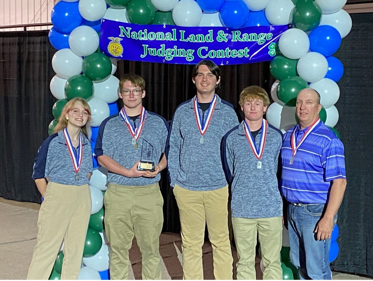 The Spink County 4-H Homesite Judging Team of Harlee Nielson, Mikael Nielson, Jackson Maynard, Brendan Nowell and coach Lance Howe stand under a blue, white and green balloon arch with a banner that says "National Land & Range Judging Contest"