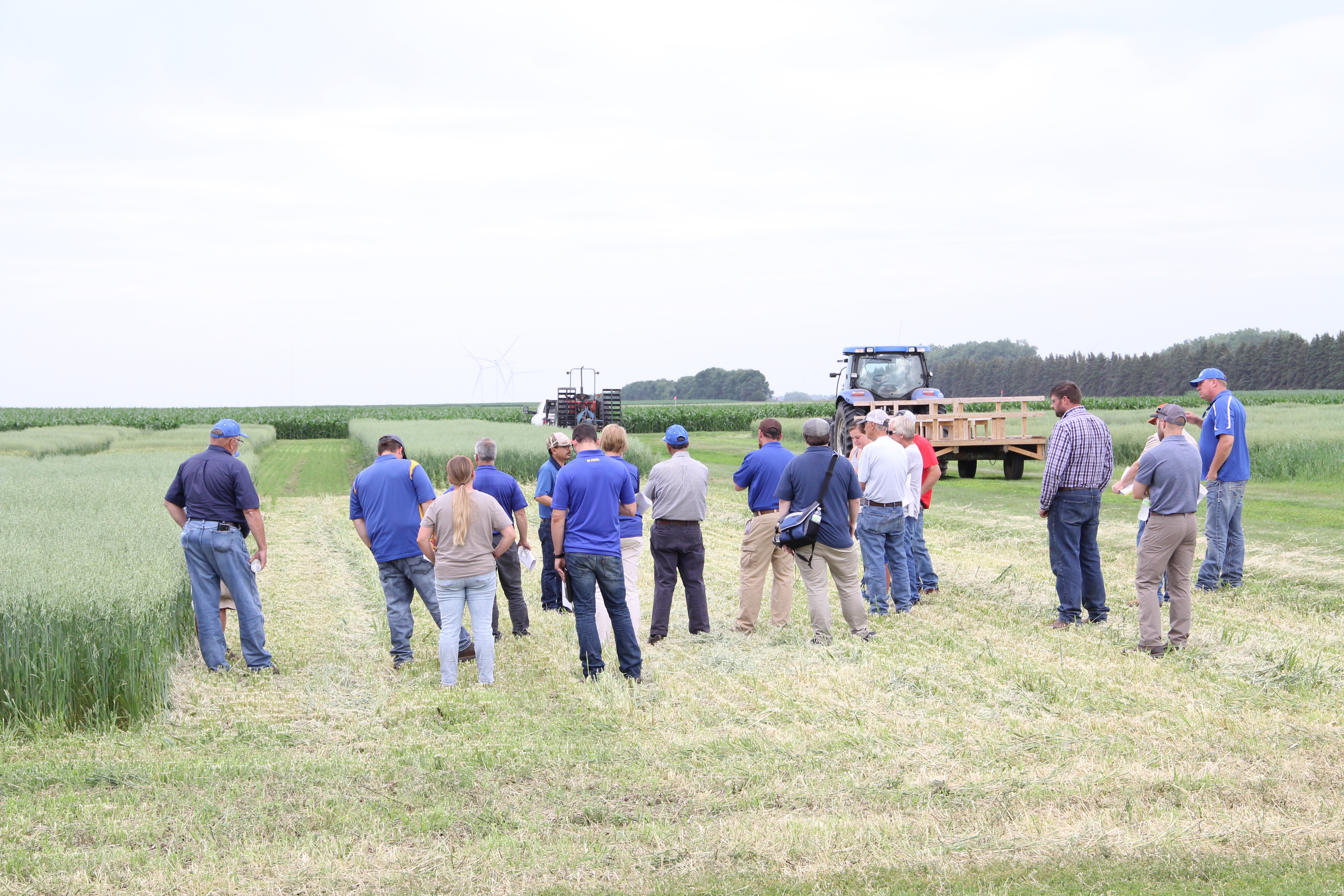 A group of people stand in a field with a combine in the background