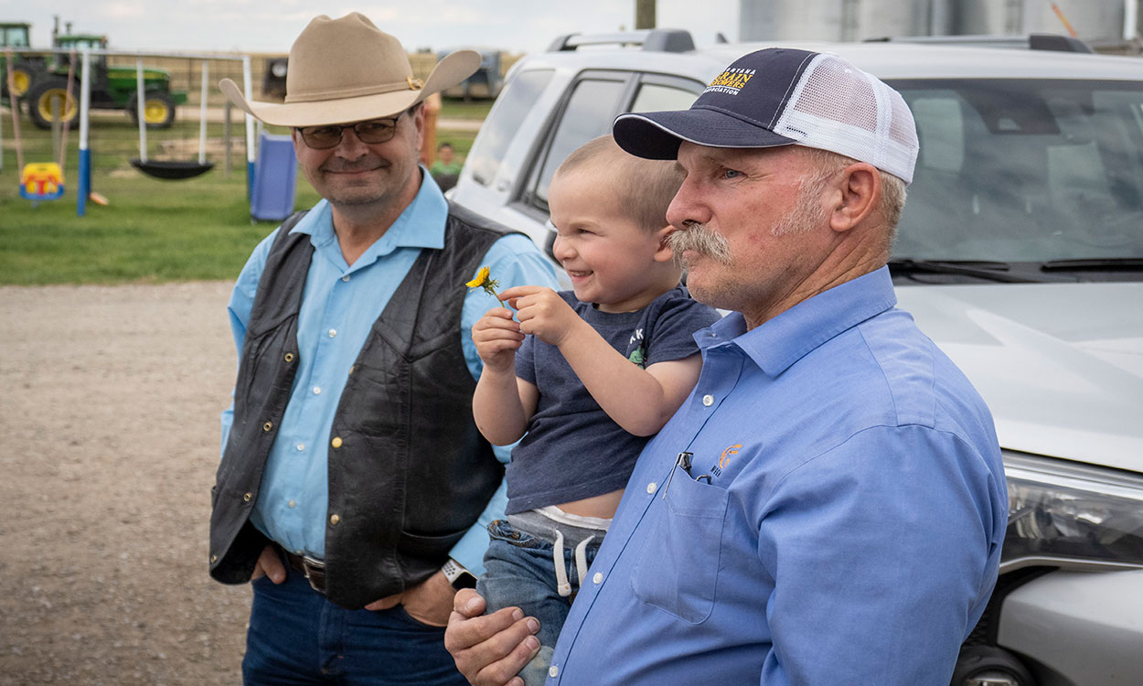 Father, son, and grandchild gathered at family farmyard.
