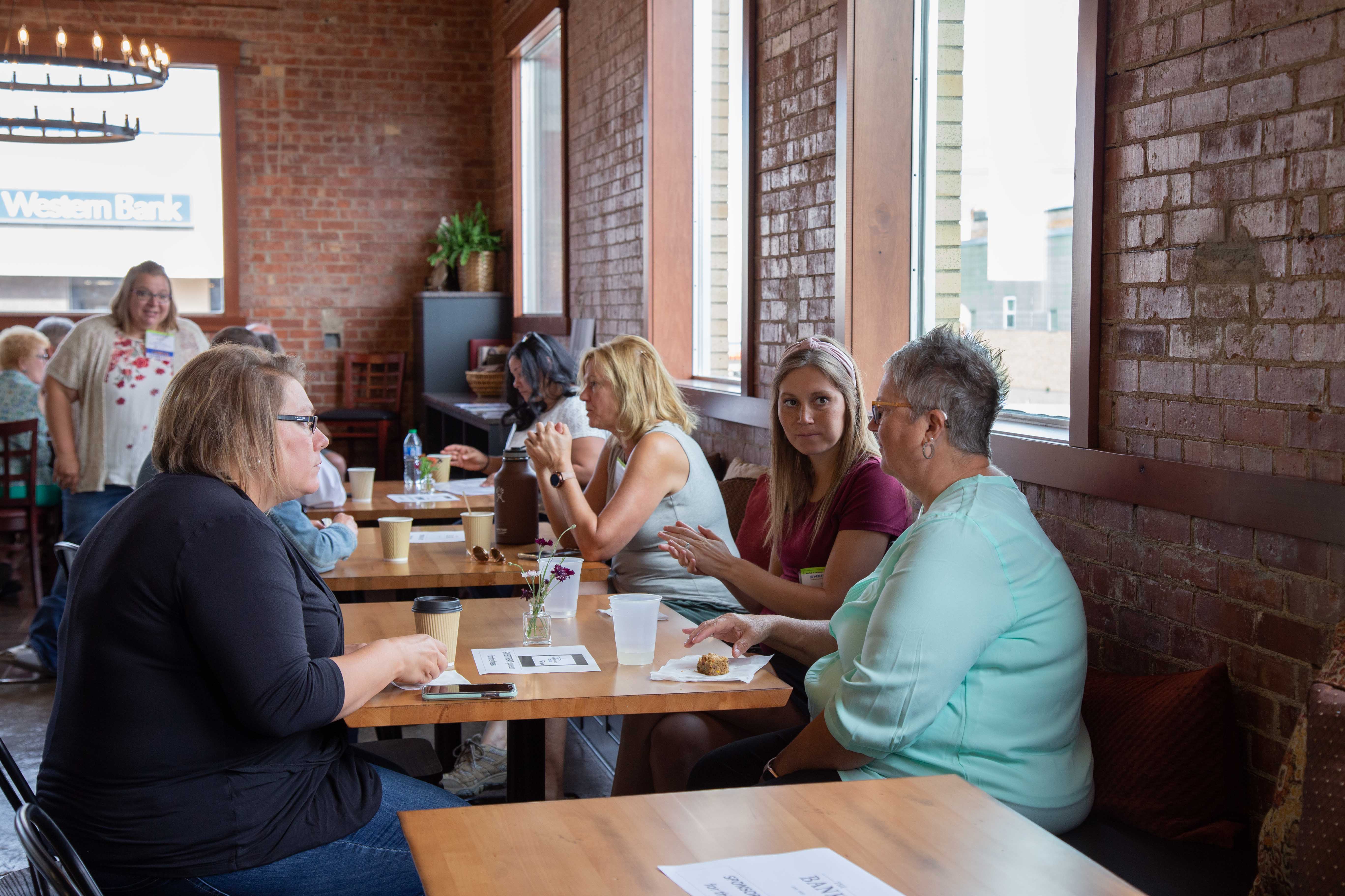 Three women sit at a booth in a small cafe.