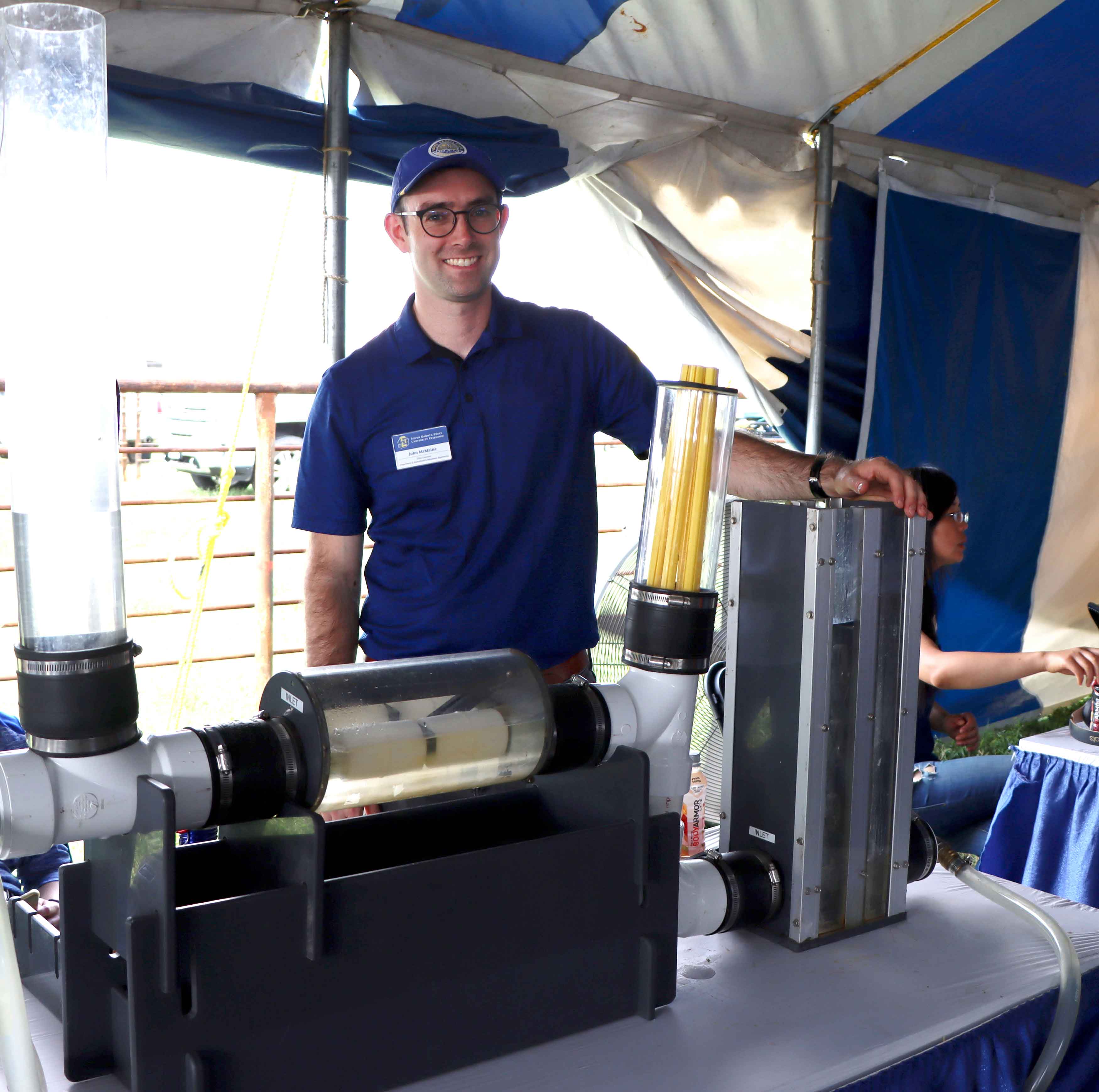 John McMaine stands smiling behind water equipment inside the SDSU Extension booth at Dakotafest