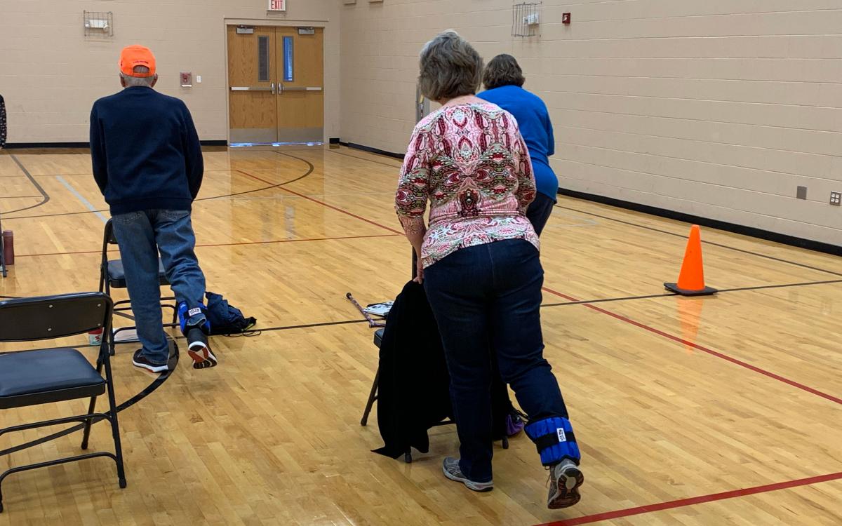 A group of older adults performing exercises in a school gymnasium.