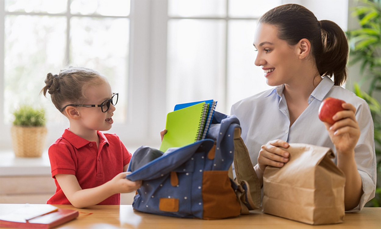 Mother and daughter packing backpack and brown lunch bag.
