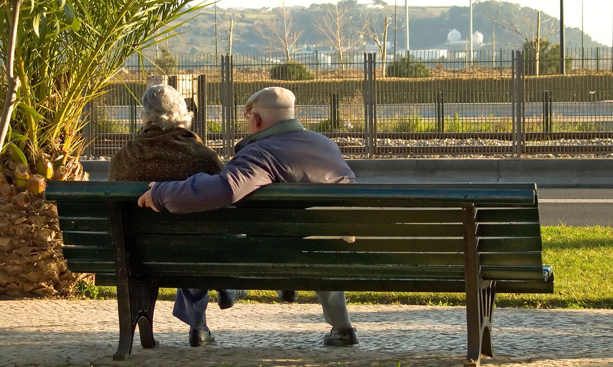 Retired couple sitting on a park bench overlooking a bluff.