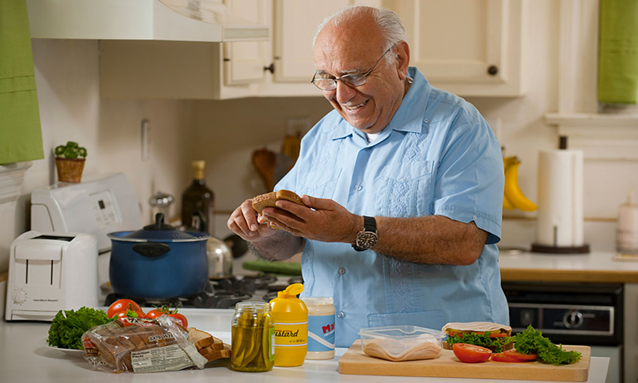 Older adult man prepares a sandwich.