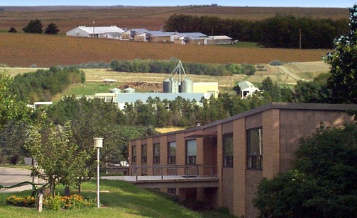 The University of Nebraska Lincoln Haskell Lab is pictured, a brown brick building in the foreground with fields and farm buildings in the background