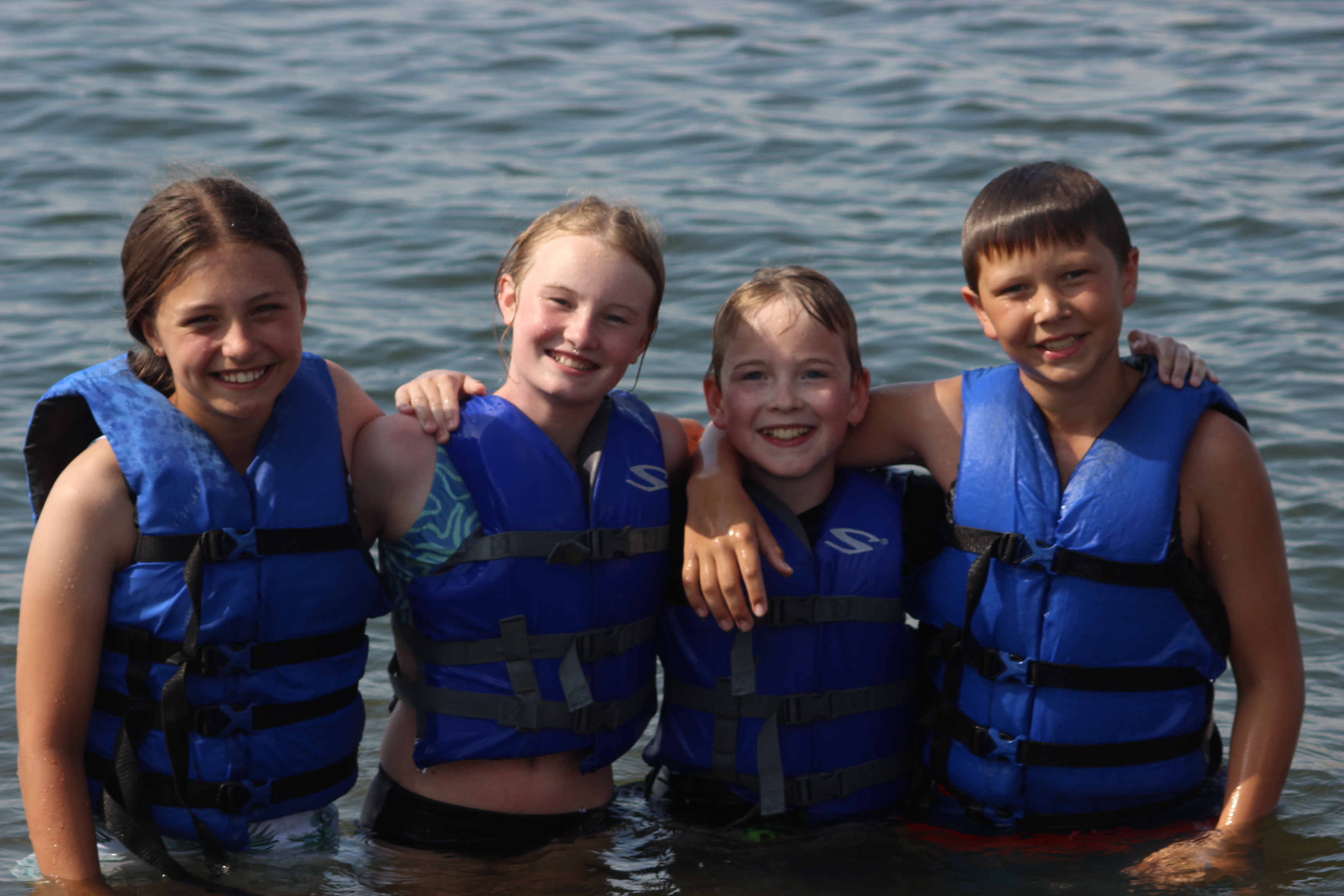 Four youth campers in lifejackets standing in the lake