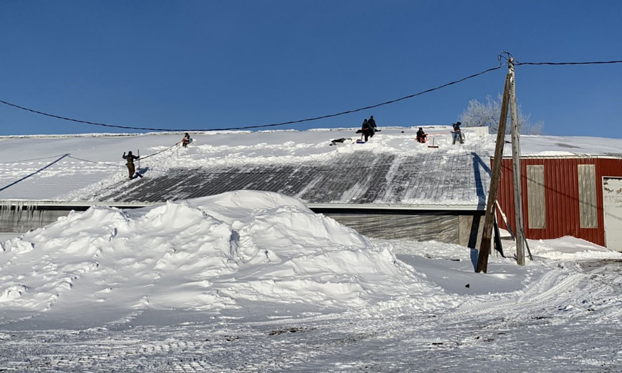 Small crew of workers removing snow from the roof of a pole barn.