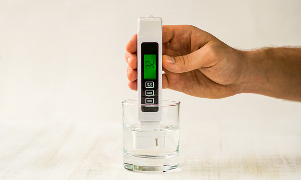 Hand holding a TDS meter in a water container.