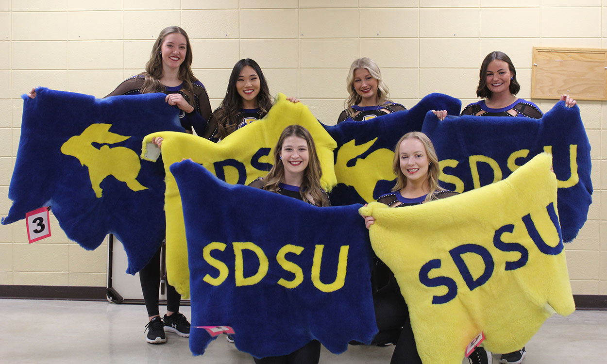 Six young women hold up blue and yellow lamb pelts emblazoned with &quot;SDSU&quot; and the Jackrabbit logo