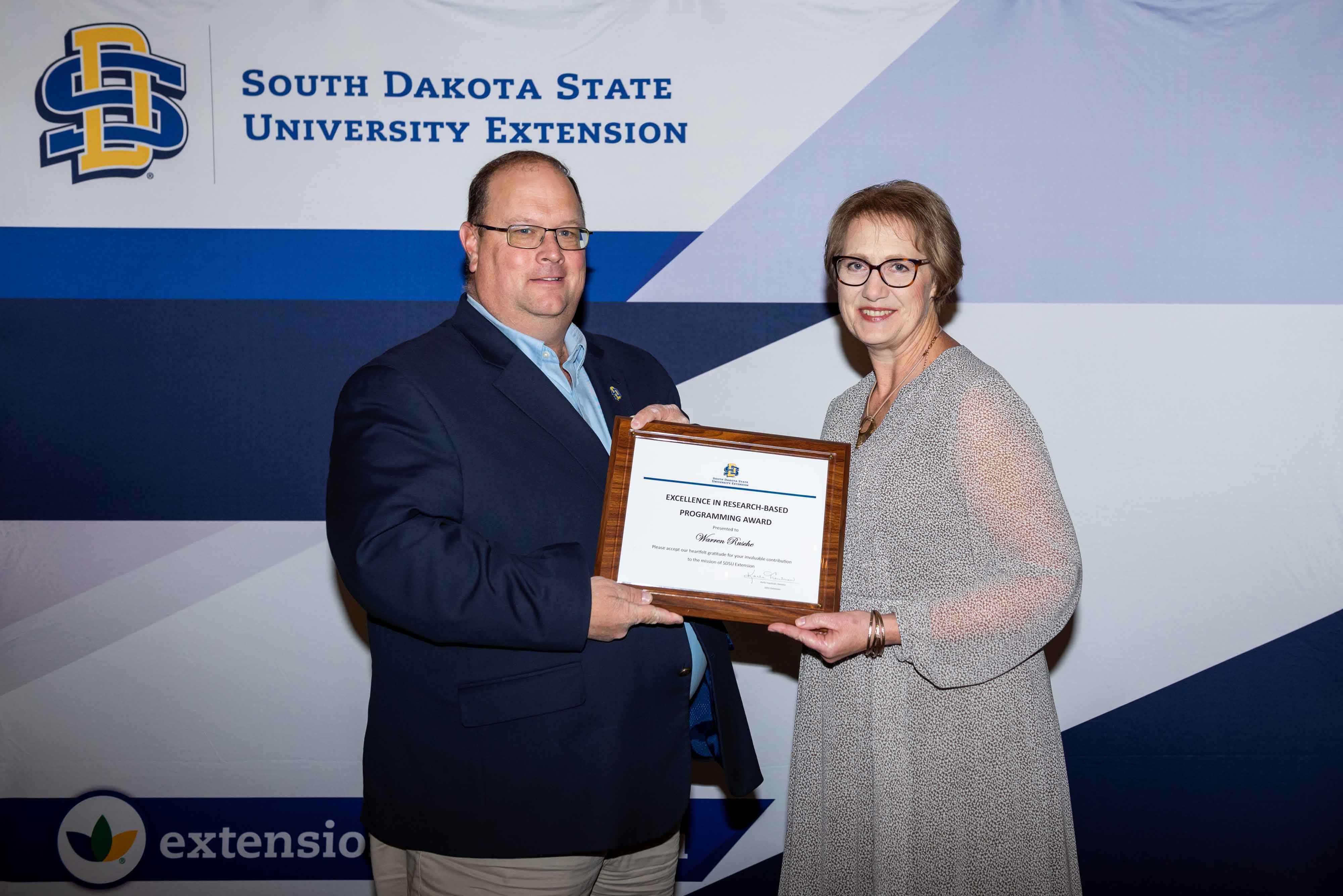 Warren Rusche smiles at the camera while accepting his award certificate from Karla Trautman
