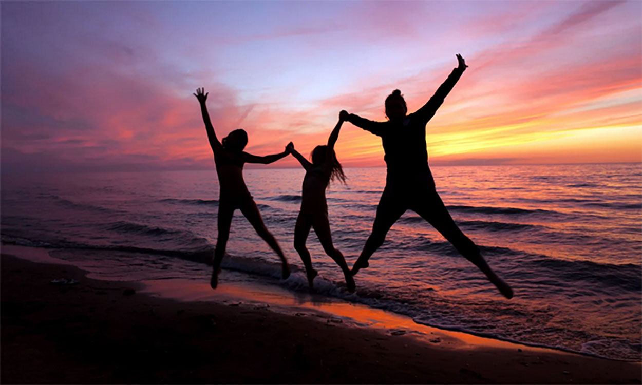 Silhouettes of three women jumping on the beach at sunset.
