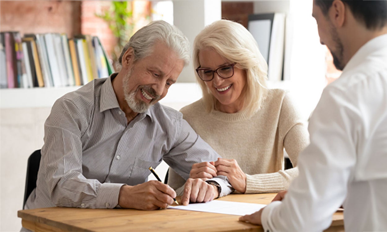 An older couple reviewing and signing paperwork with a health care professional.