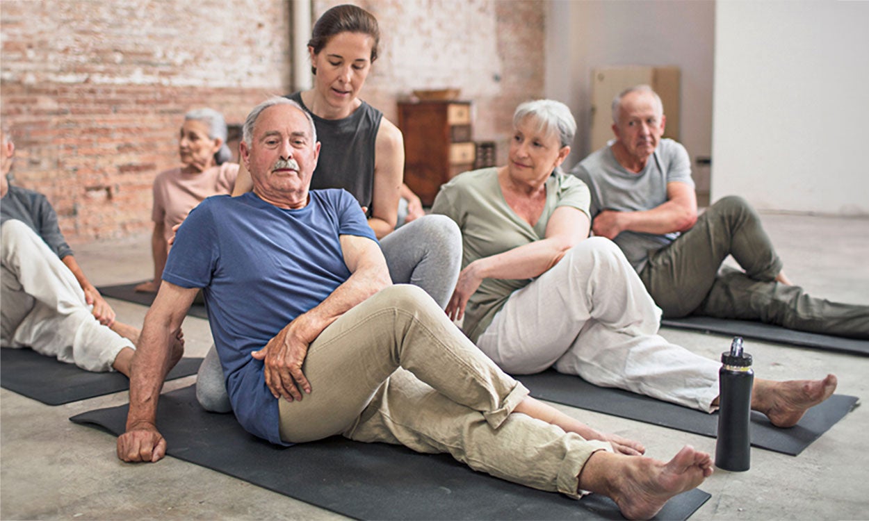 Yoga instructor helping a group of older adults with stretching exercises.