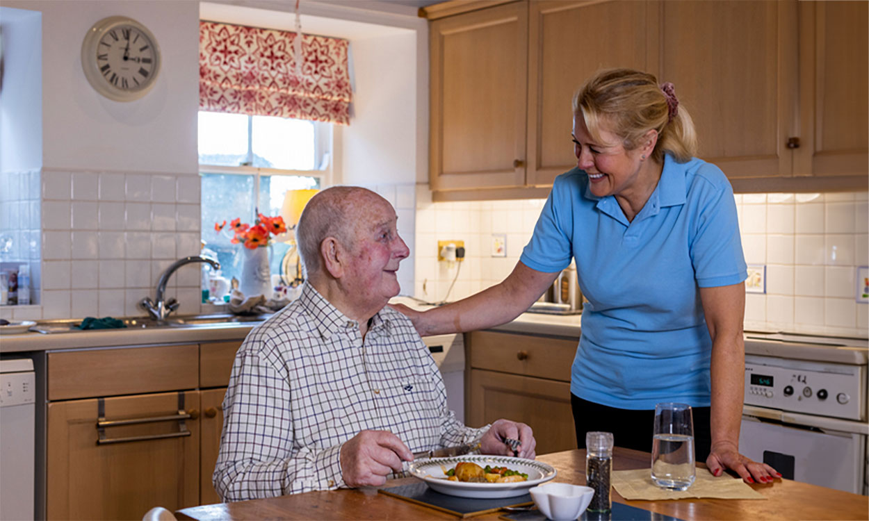 Caregiver serving a home-cooked meal to an older adult male.
