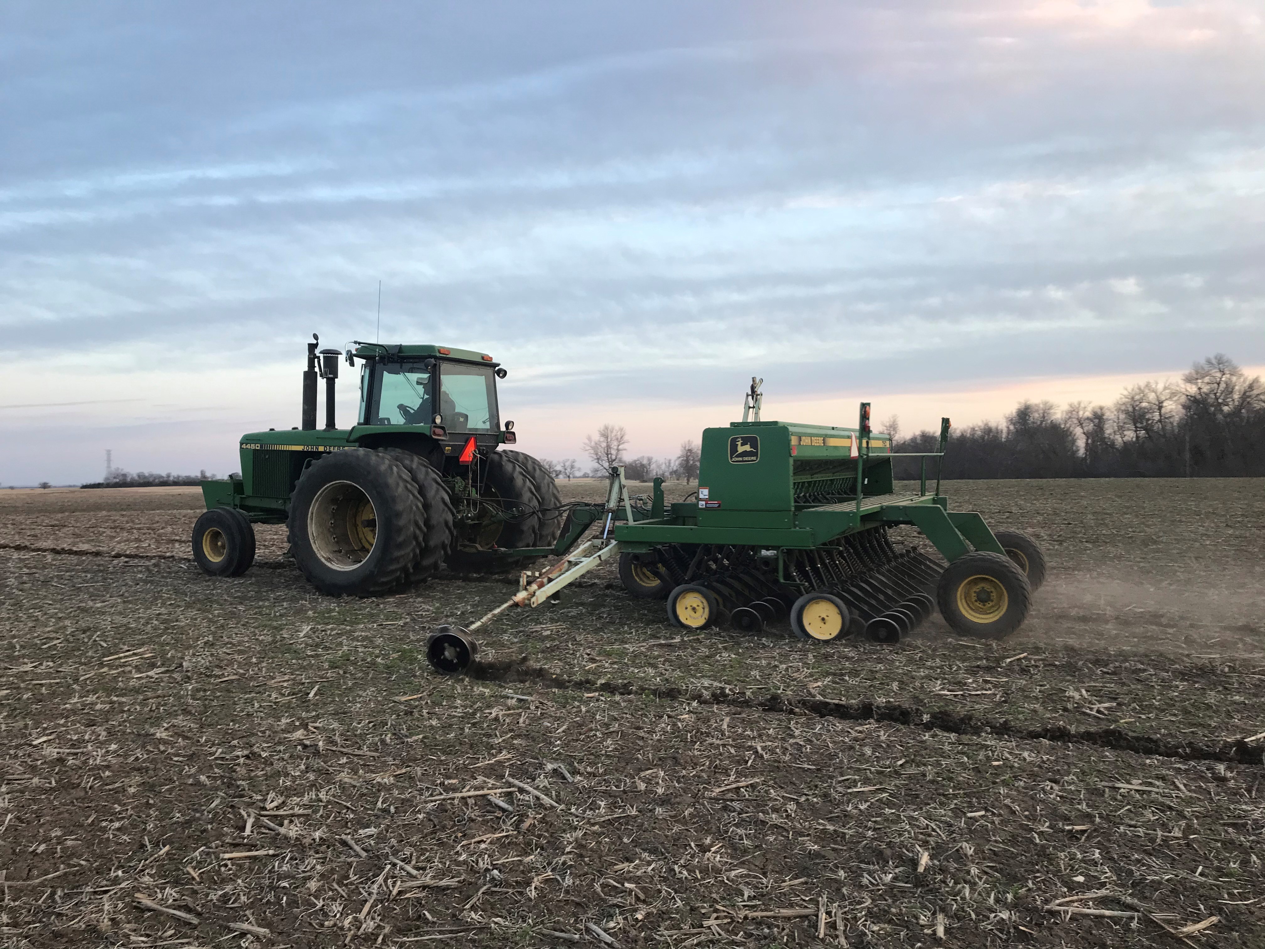 A green tractor pulls a planter to plant oats in a field