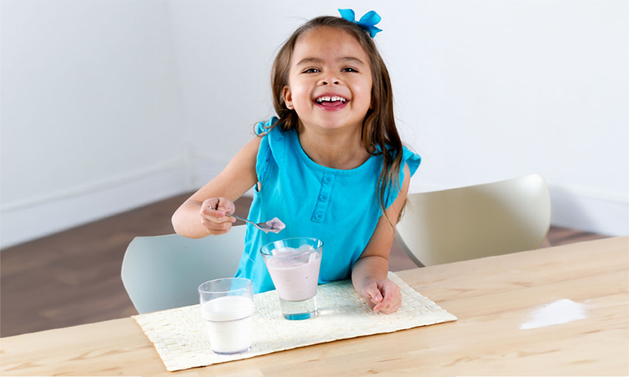 Young girl eating yogurt at a kitchen table.
