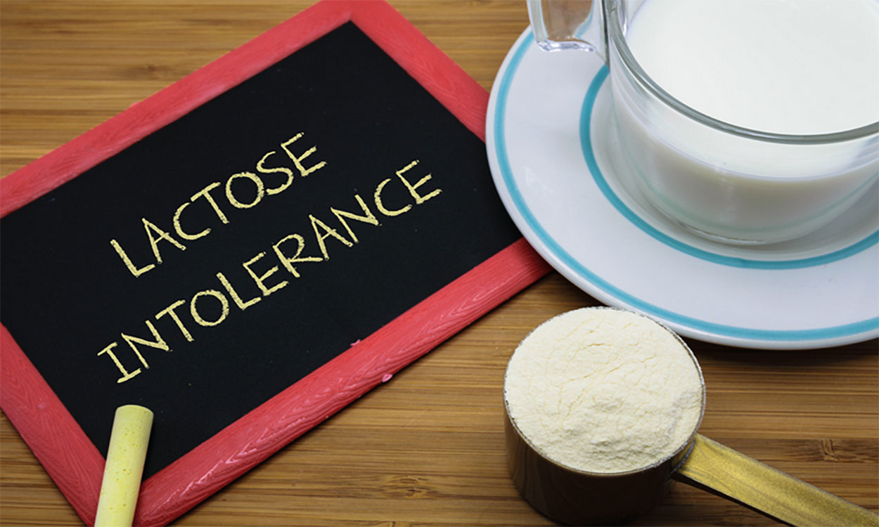 Chalkboard with the words “Lactose Intolerance” written on it next to a glass of milk.