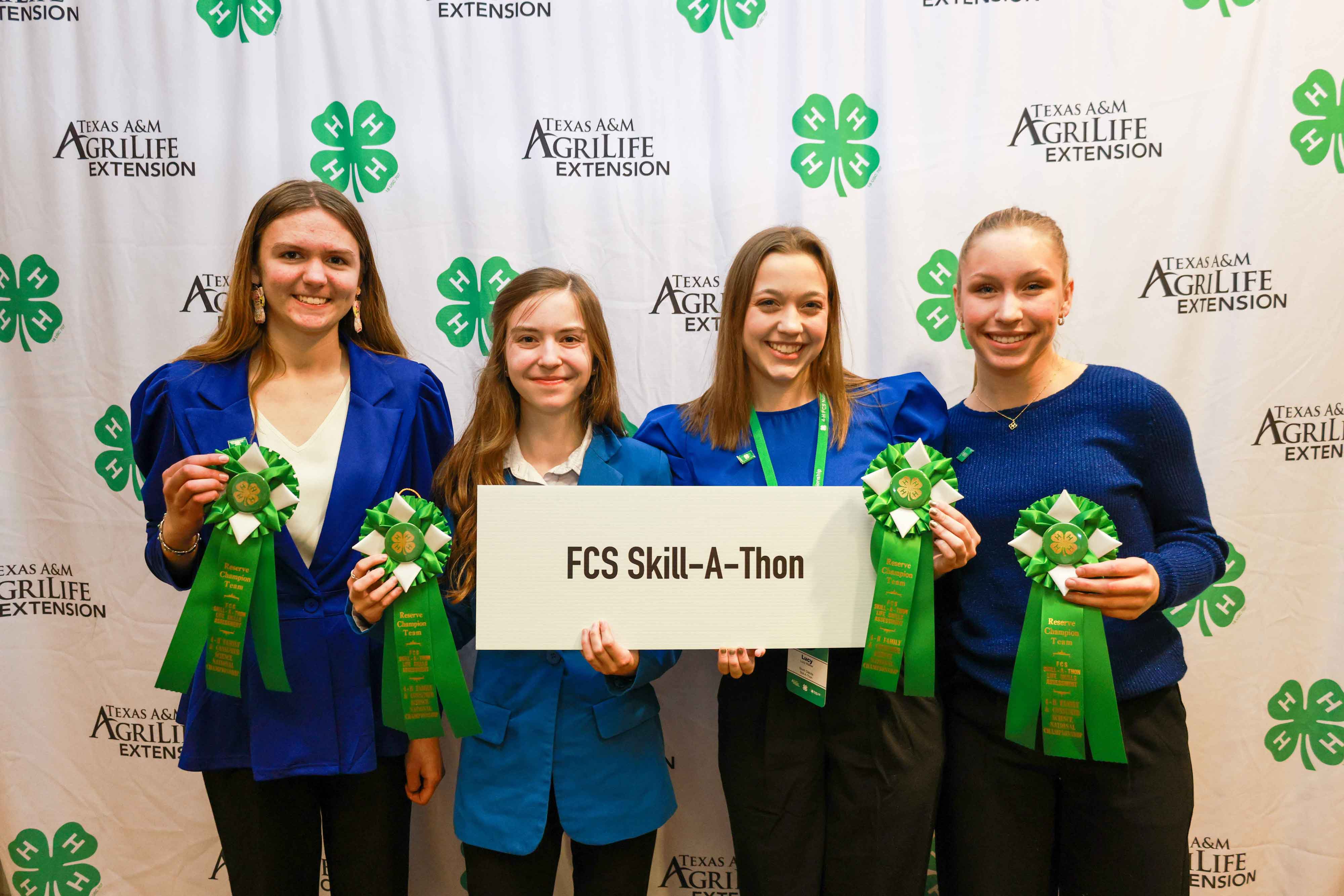 The four members of the South Dakota FCS Skill-a-Thon stand with their green ribbons and holding a white sign that says FCS Skill-a-Thon at the 2024 National 4-H FCS Championship and Conference