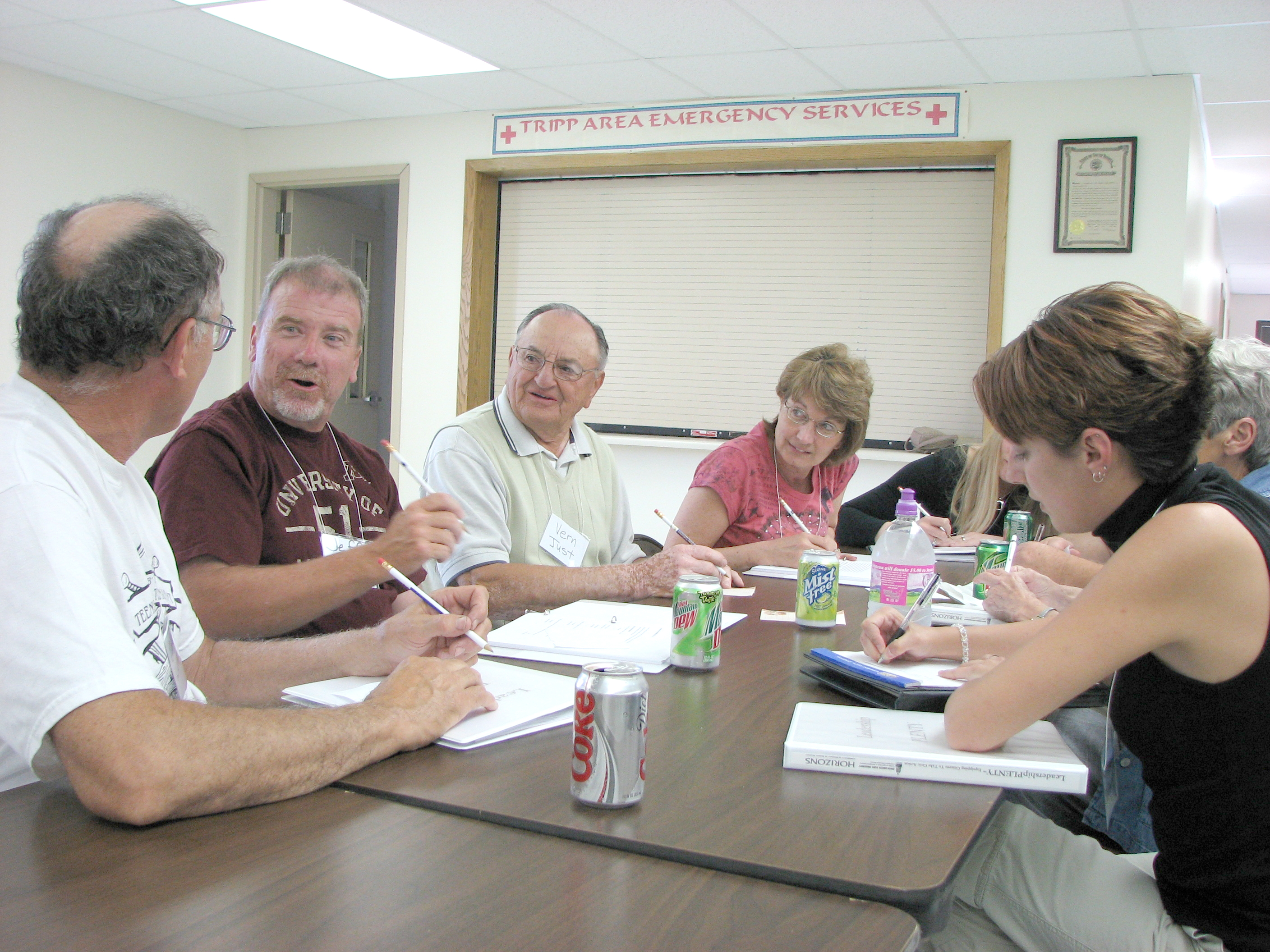 About six people sit around a table in a community room with notebooks and pens
